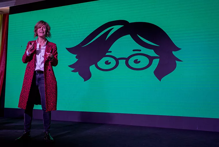 Mujero sobre un escenario hablando con una ilustración de ella de fondo en la pantalla